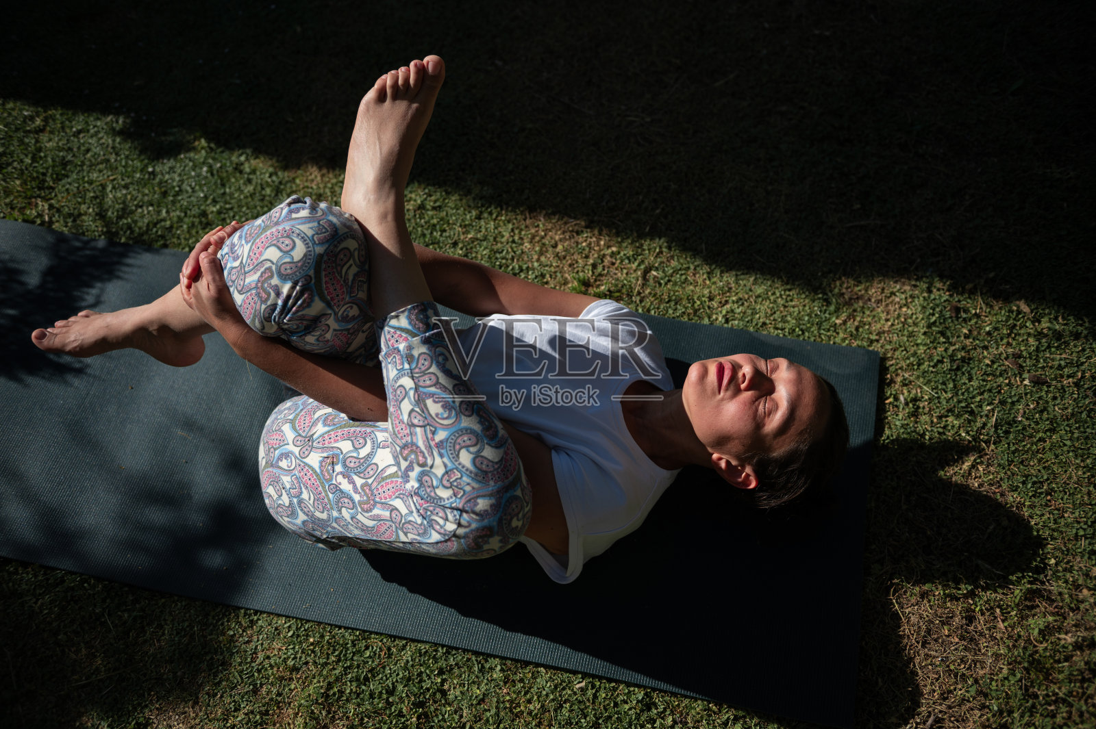 一名妇女在户外的垫子上晒太阳练习瑜伽，享受宁静的时刻照片摄影图片