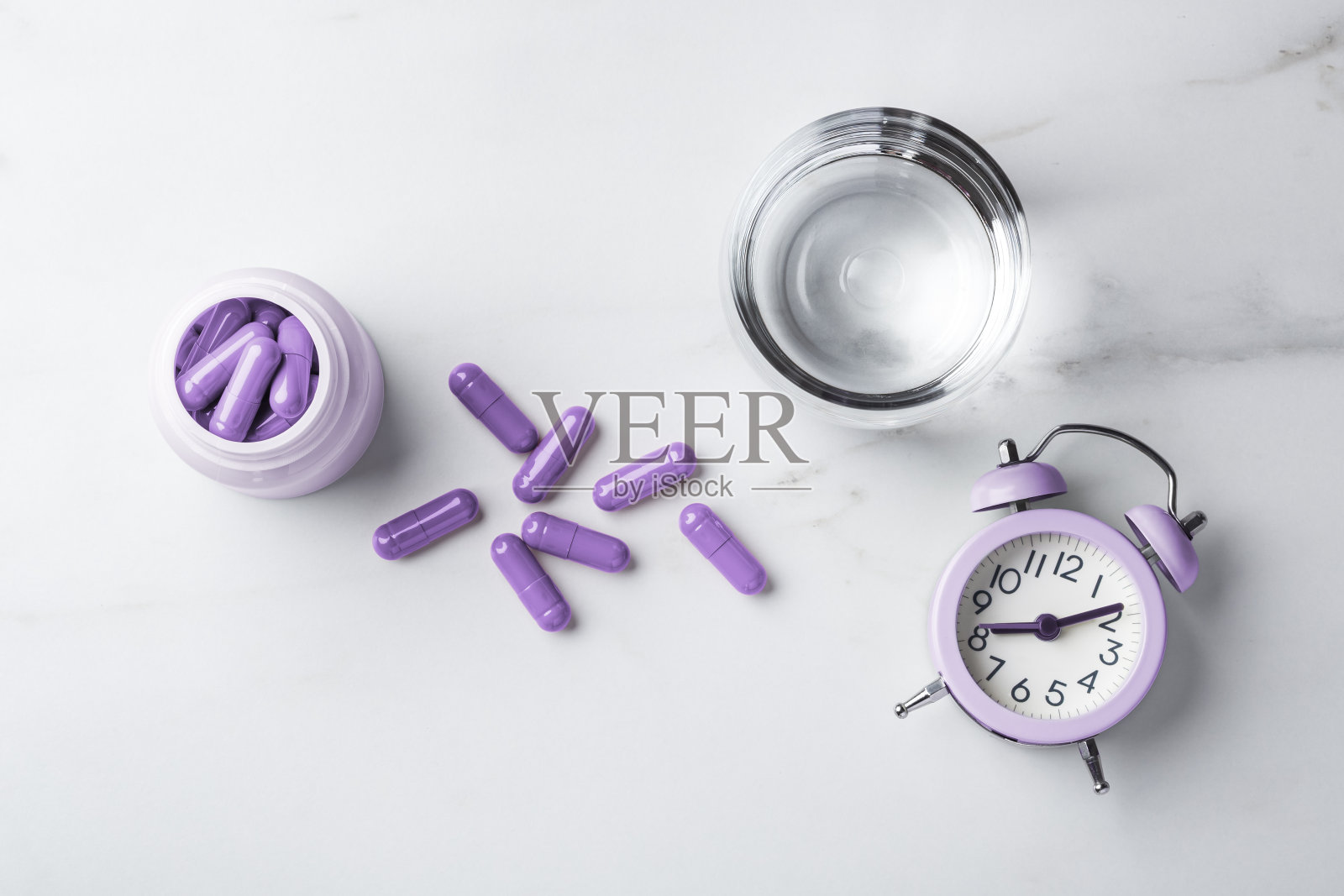 安眠药概念，紫色胶囊和瓶子，白色桌子上的一杯水和闹钟照片摄影图片