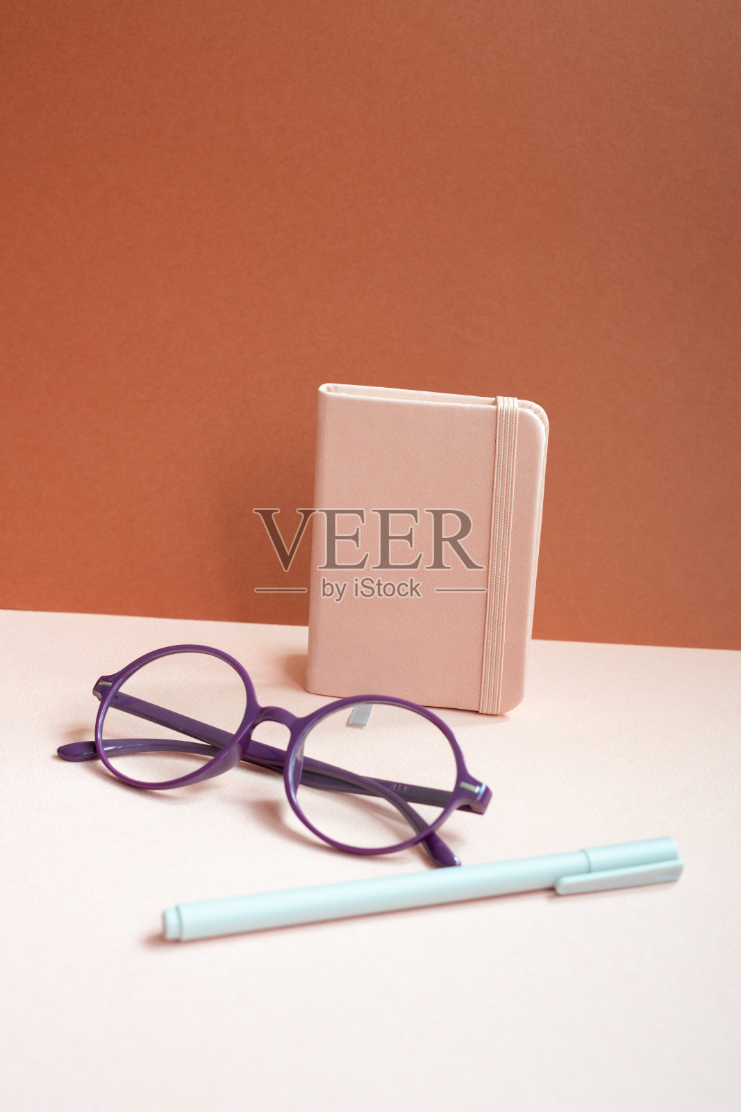 粉红色的桌子上放着日记、笔记本、钢笔、眼镜。红色的背景照片摄影图片