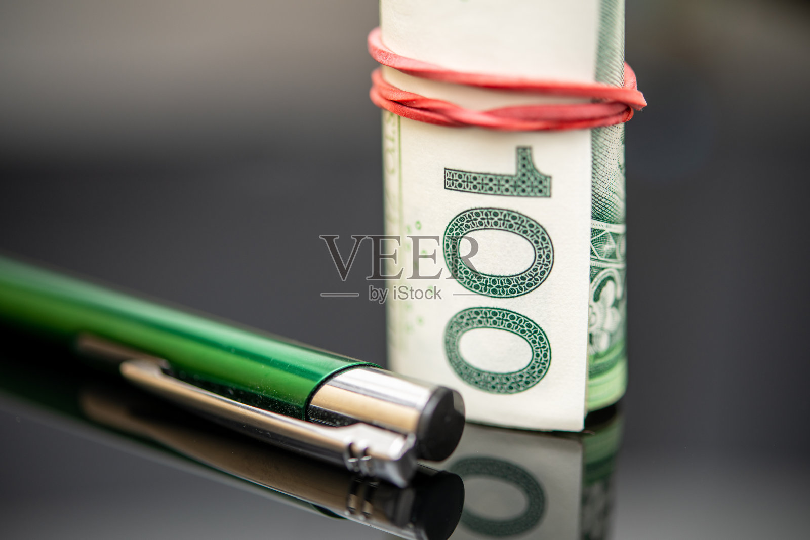 100波兰兹罗提钞票卷的特写，用橡皮圈固定在反光表面的绿笔旁照片摄影图片