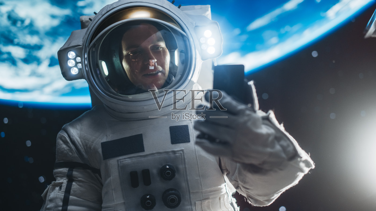 一个穿着太空服的人在外太空一边抓着卫星一边随意地打电话。宇航员在智能手机上与任务控制人员、家人或同事进行视频通话照片摄影图片