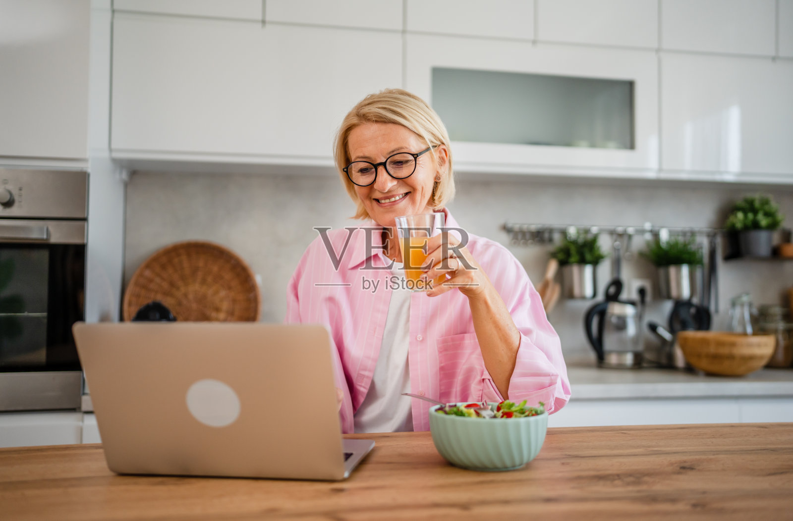 一个女人在厨房一边喝果汁一边用笔记本电脑工作照片摄影图片