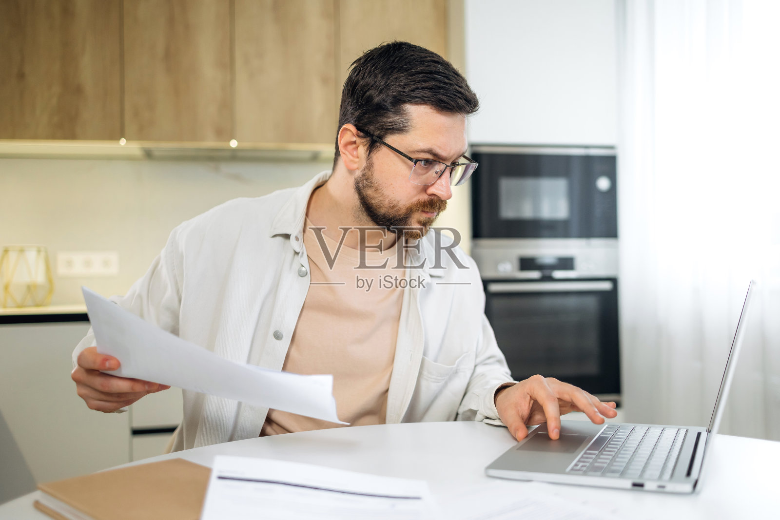 年轻人戴着眼镜阅读信件和文件，坐在桌旁拿着笔记本电脑拿着文件、纸质通知照片摄影图片