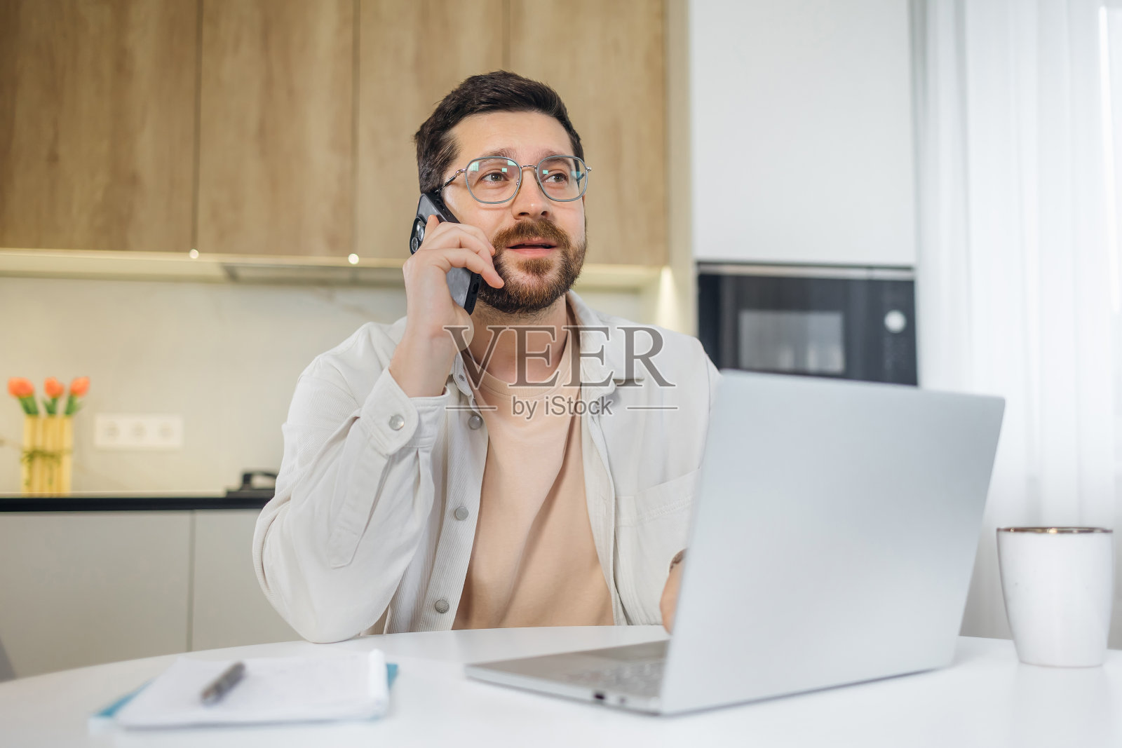 软件设计师正在电话里和客户讨论一个新项目。一个有创造力的商人在家里用笔记本电脑在厨房工作照片摄影图片