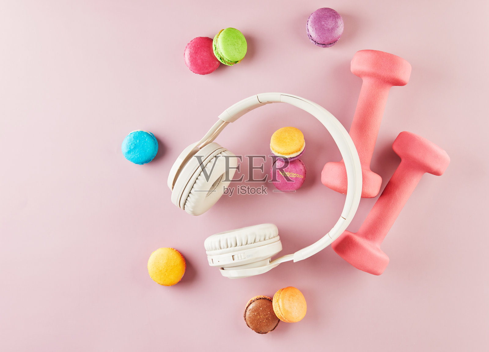 粉色背景上的彩色马卡龙、耳机和哑铃照片摄影图片