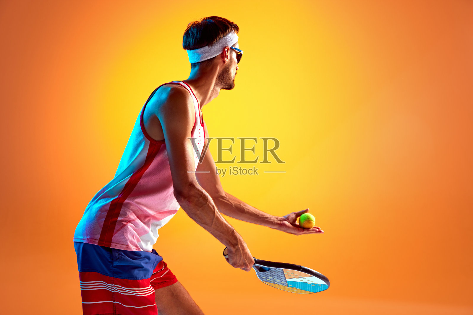 戴着太阳镜、身穿运动服，在霓虹灯下专注地打沙滩网球的男人照片摄影图片