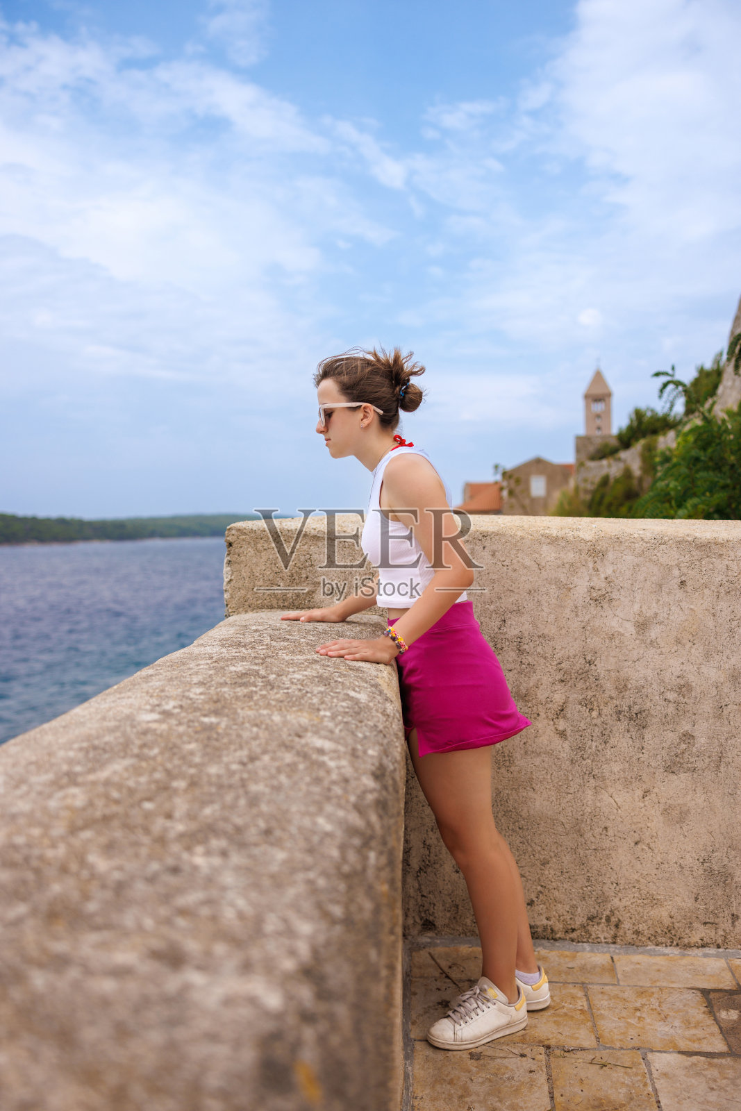十几岁的女孩穿着夏装站在石砌的台墙边，看着大海照片摄影图片