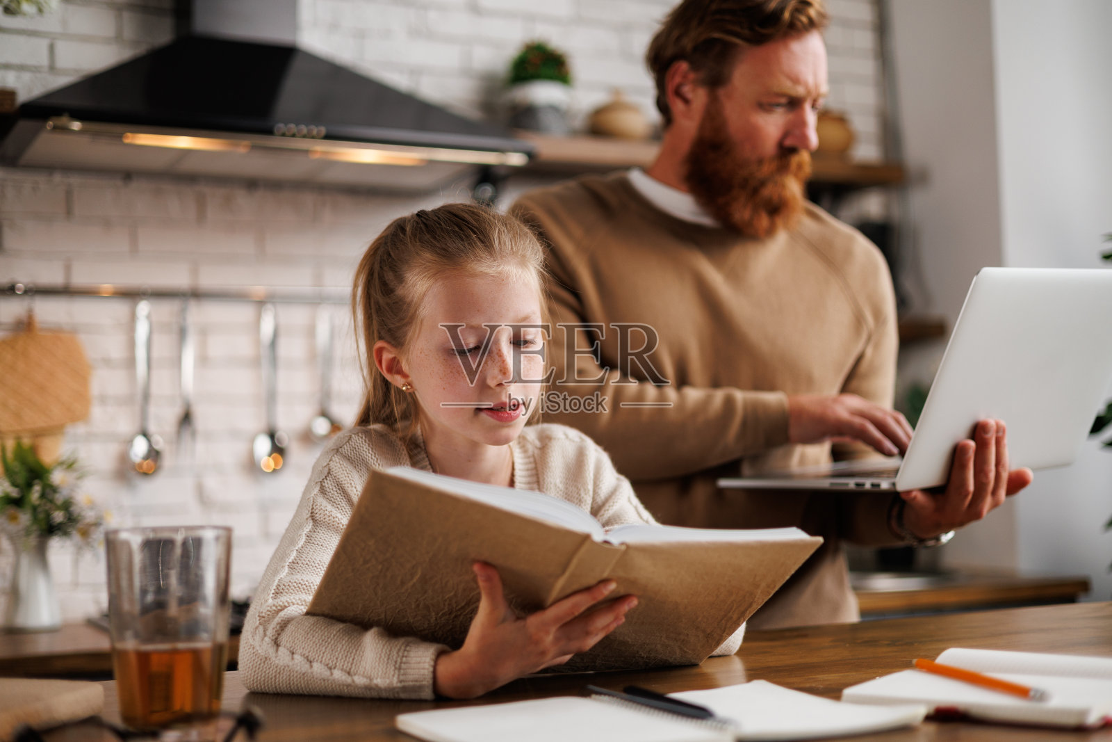 孩子在厨房用笔记本电脑和笔记本在爸爸身边看书照片摄影图片