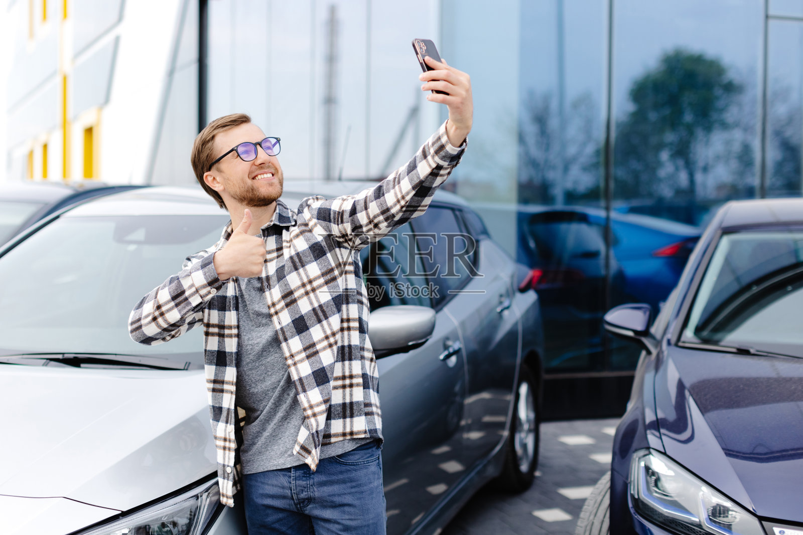 买了新车后用智能手机自拍的快乐男人。该男子通过电话视频链接展示了购买的汽车照片摄影图片