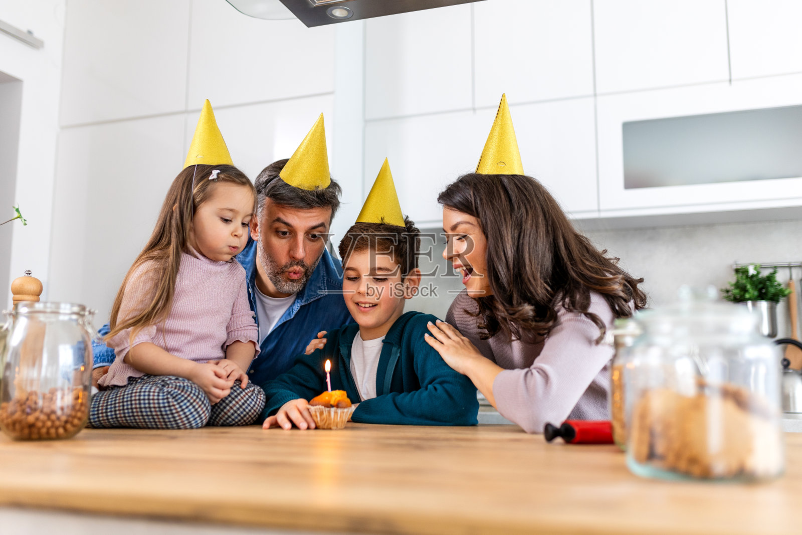 父亲在厨房吹灭生日蛋糕上的蜡烛。幸福的一家人在厨房里一起庆祝生日照片摄影图片