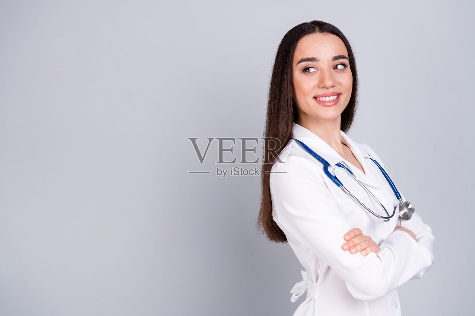 照片中可爱的女儿科医生穿着白色的医生长袍，在灰色的背景上显得空旷孤立。照片摄影图片