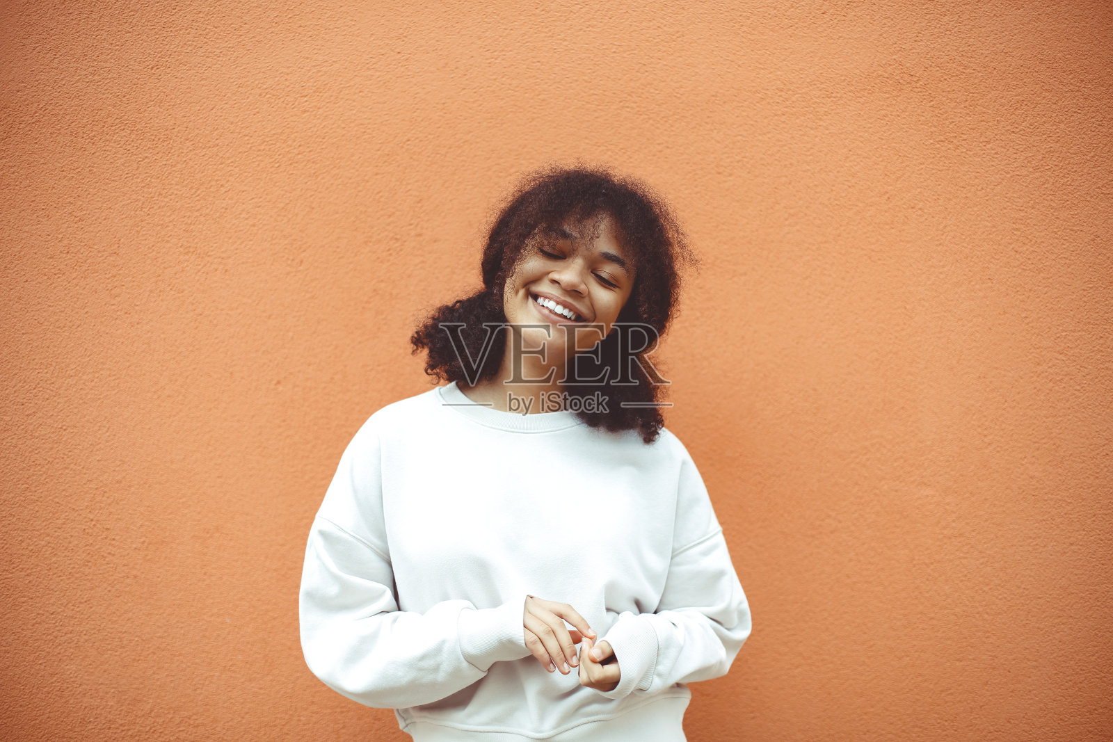 纯粹的幸福。快乐卷曲的非裔美国女孩闭着眼睛对着橙色的墙照片摄影图片