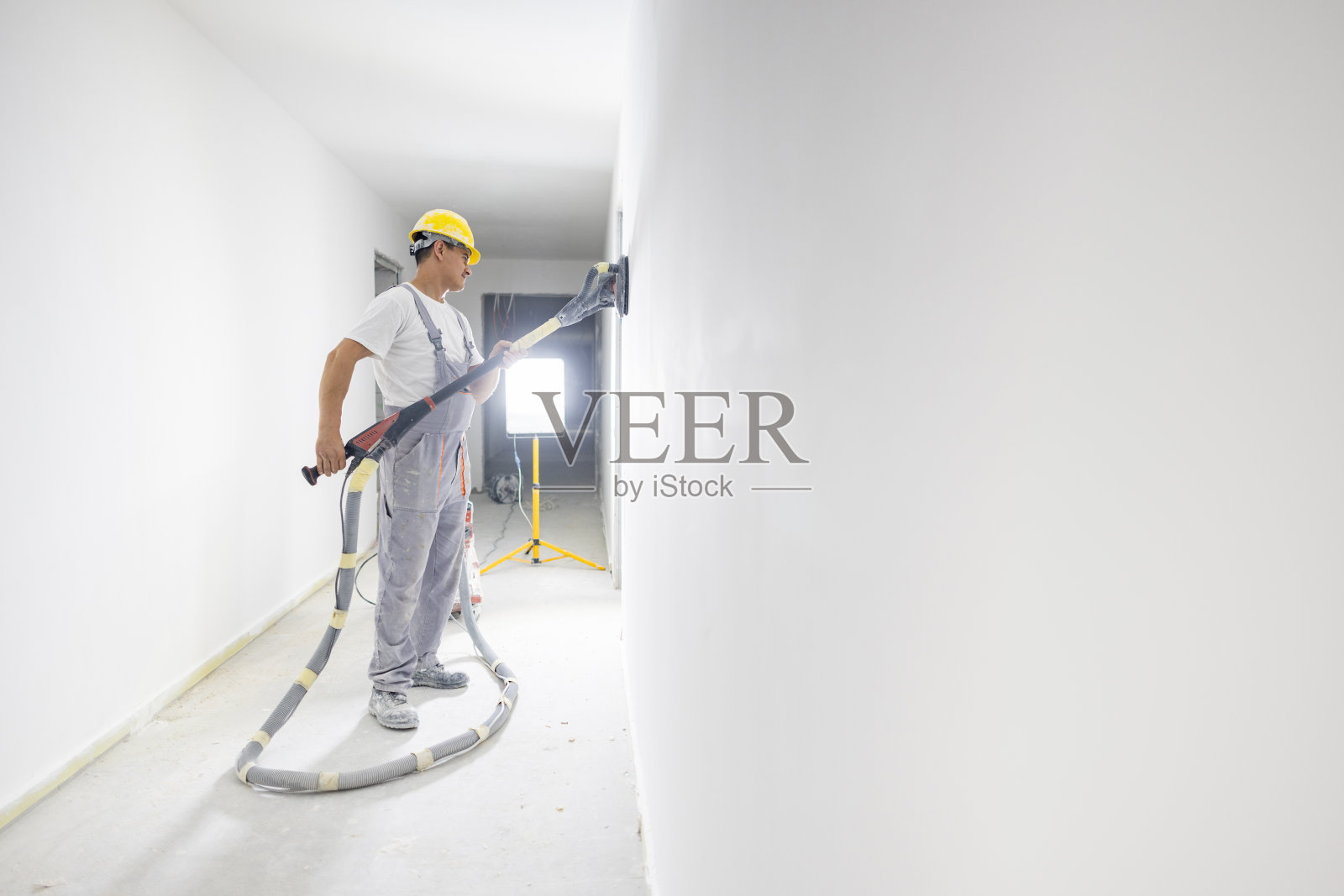 在一个建筑工地，年轻的白人男性建筑工人正在使用砂光真空机照片摄影图片