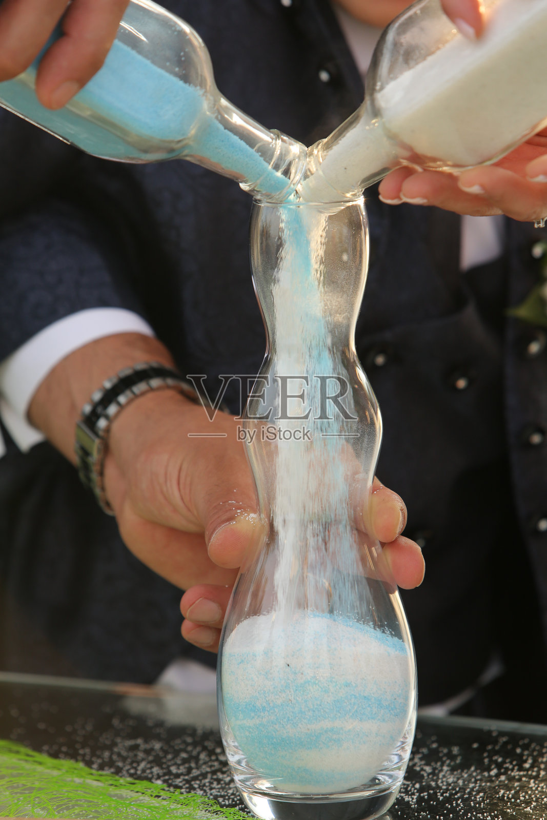 新娘和新郎在婚礼上把不同颜色的沙子倒进一个玻璃杯里照片摄影图片