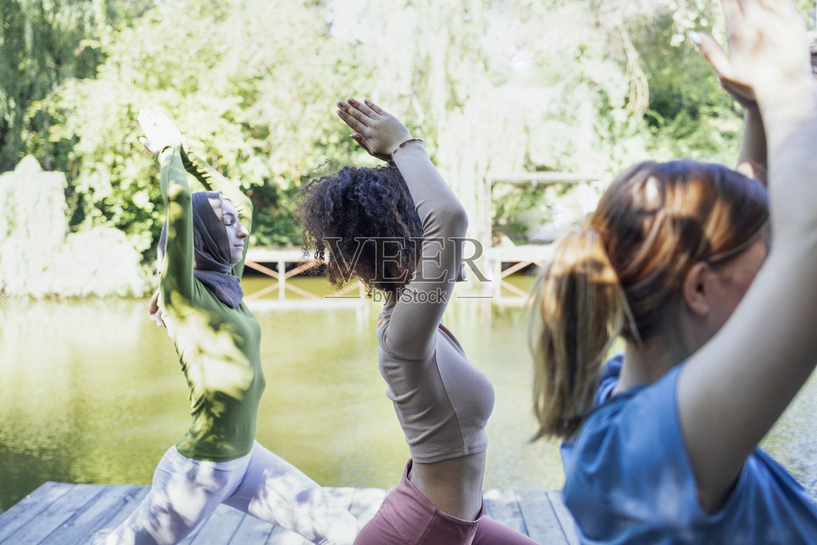 年轻而积极的女孩喜欢运动。戴着头巾的穆斯林、非洲裔美国人和白人女性正在公园里做伸展运动。照片摄影图片