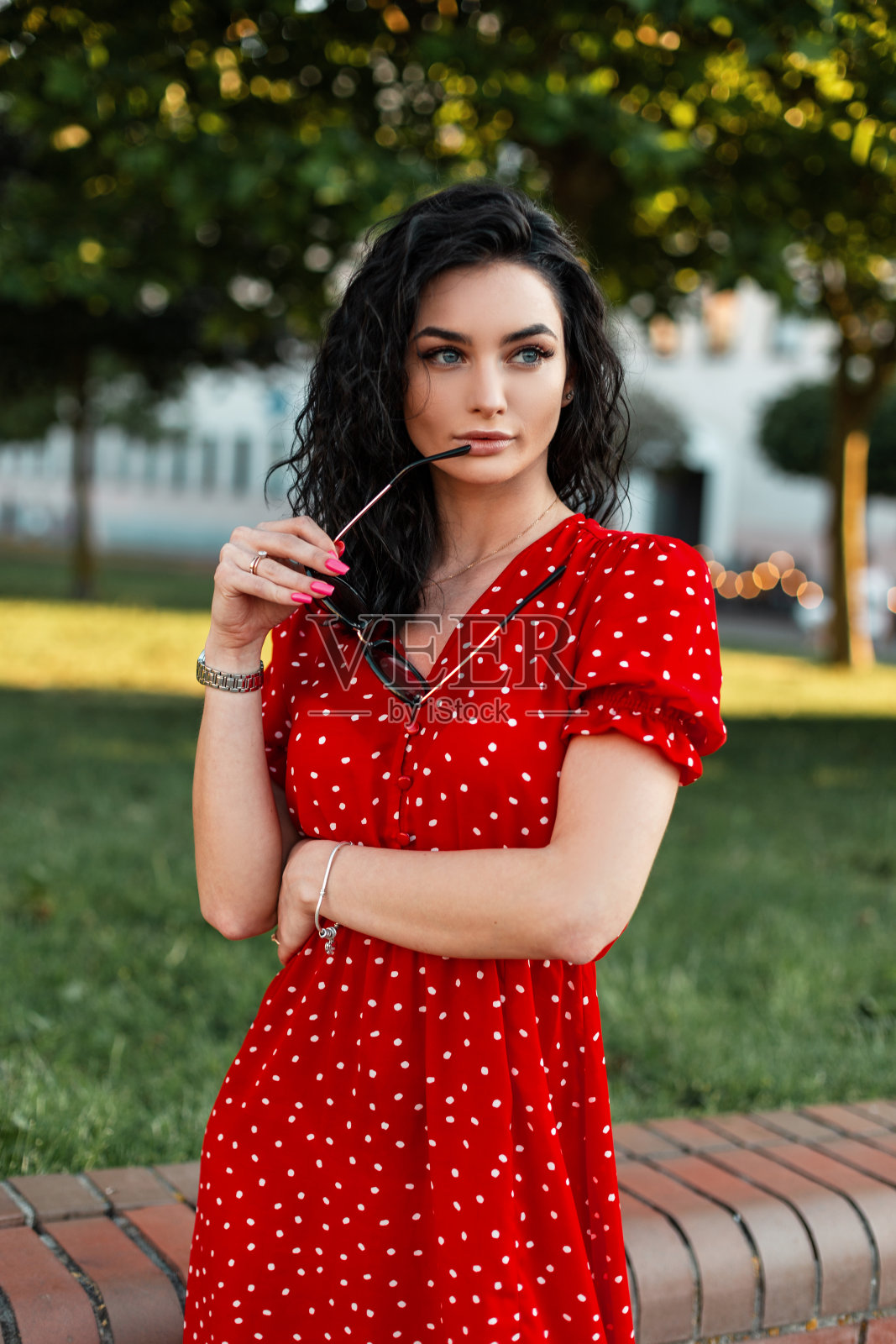 漂亮的年轻女子穿着时尚复古的红色连衣裙，戴着太阳镜走在镇上的街上照片摄影图片