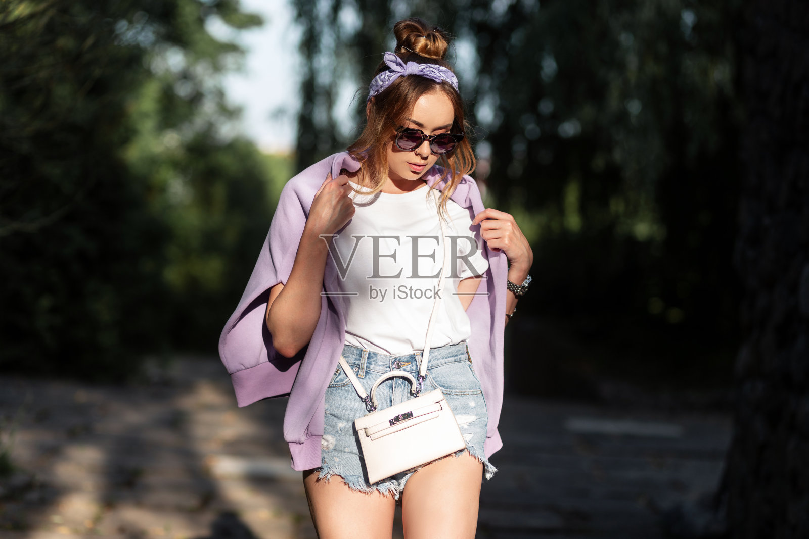 时尚的美女，戴着太阳镜，戴着头巾，穿着时尚的休闲装，带着手提包走在户外照片摄影图片
