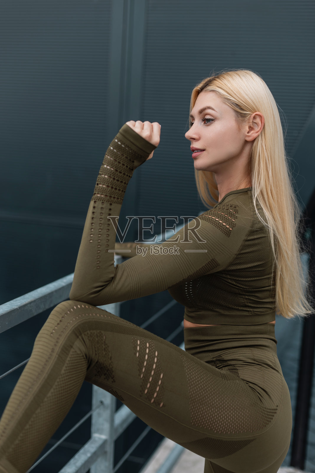 时尚运动肖像，一个美丽的健身金发女孩，长发和健康苗条的身体，在时尚的绿色运动服装在街上摆姿势照片摄影图片