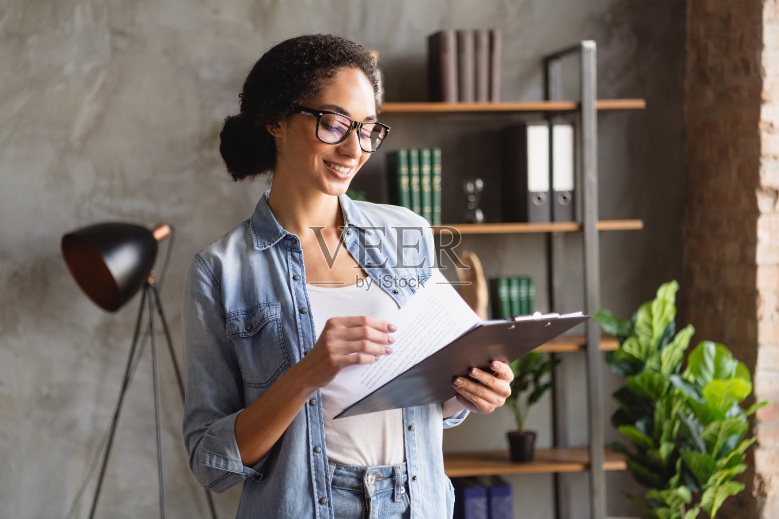 照片开朗可爱的成功女性穿着时髦的牛仔服装阅读简历简历文件现代办公空间室内照片摄影图片