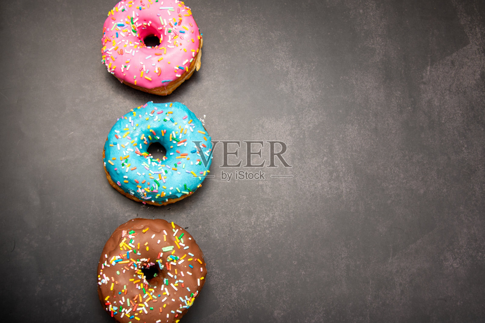 美味的甜点。粉色、蓝色和巧克力甜甜圈，上面撒着五颜六色的糖屑。照片摄影图片