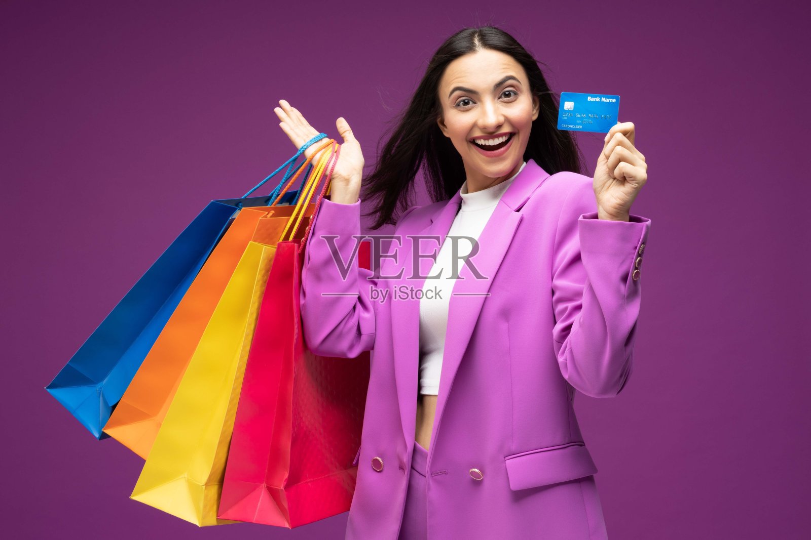 她的肖像，她漂亮的穿着漂亮的迷人的可爱的豪华漂亮开朗的女孩拿着信用卡与购物袋孤立的紫色背景股票照片照片摄影图片