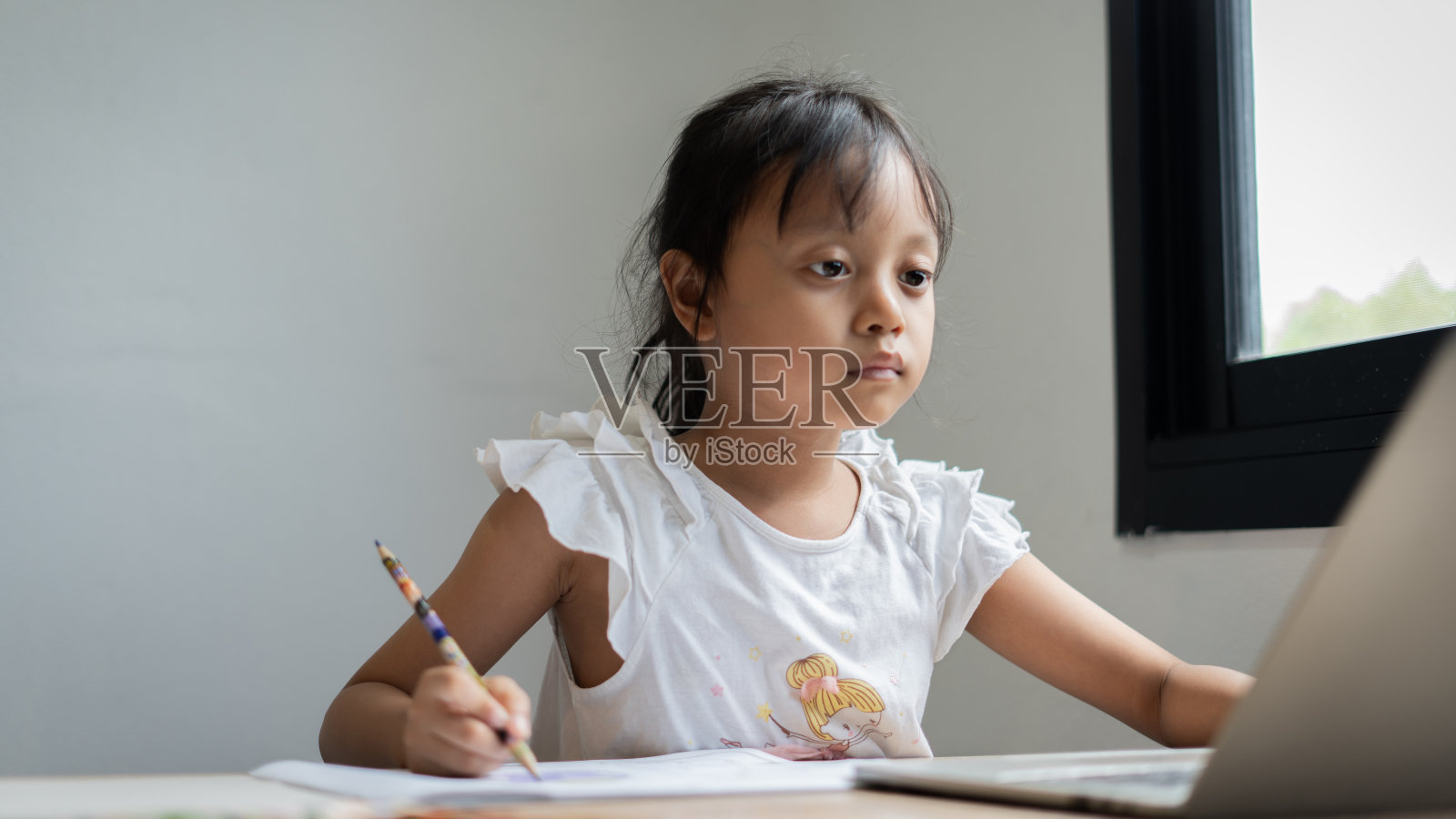 年轻女孩坐在书桌前用笔记本电脑和铅笔写字照片摄影图片