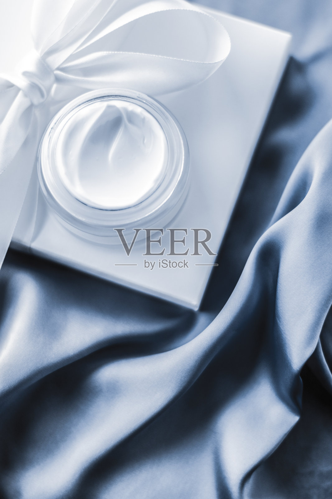 柔软的蓝色丝绸上的保湿美容面霜和礼盒照片摄影图片