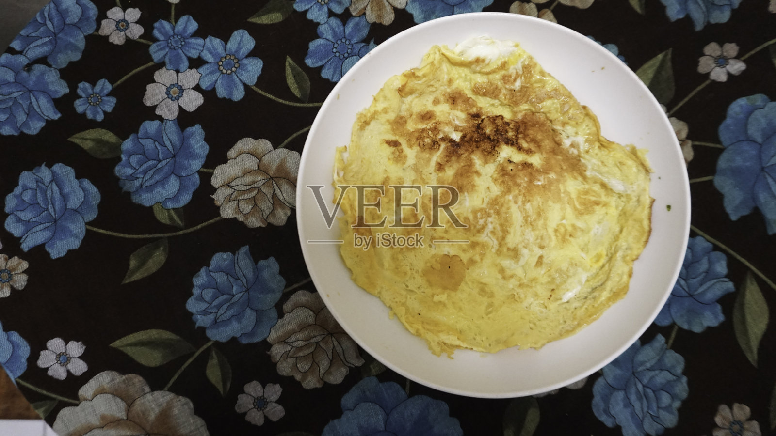 自制的煎蛋卷或telur dadar放在一个白色的盘子里，背景是花桌布照片摄影图片