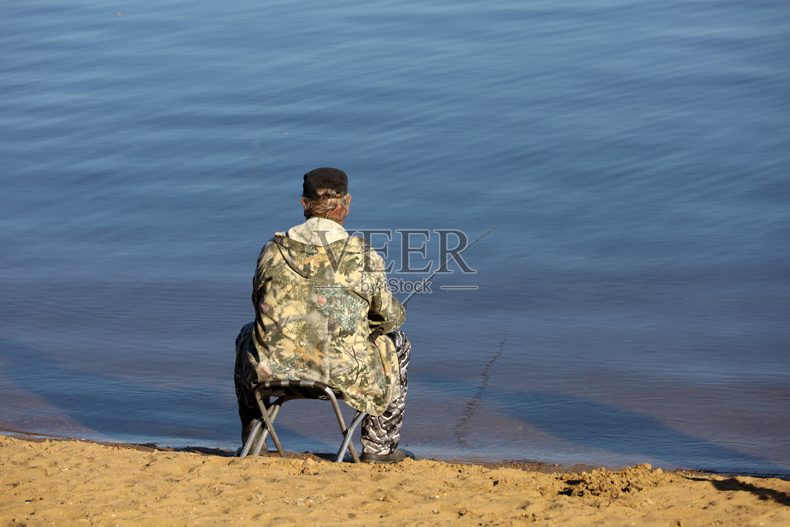 渔夫拿着鱼竿坐着，后景。春天，人们在河边垂钓照片摄影图片