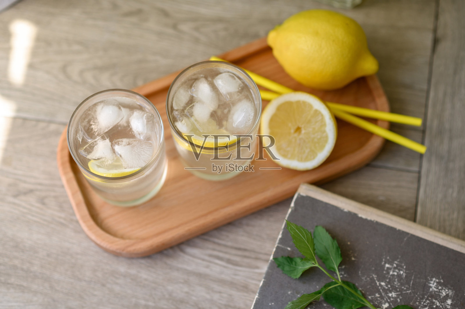 两杯加冰柠檬水的饮料放在木制托盘上，配上黄色的柠檬和吸管，中性米色的桌子背景，俯视图，柔和的选择性聚焦，生活方式照片摄影图片
