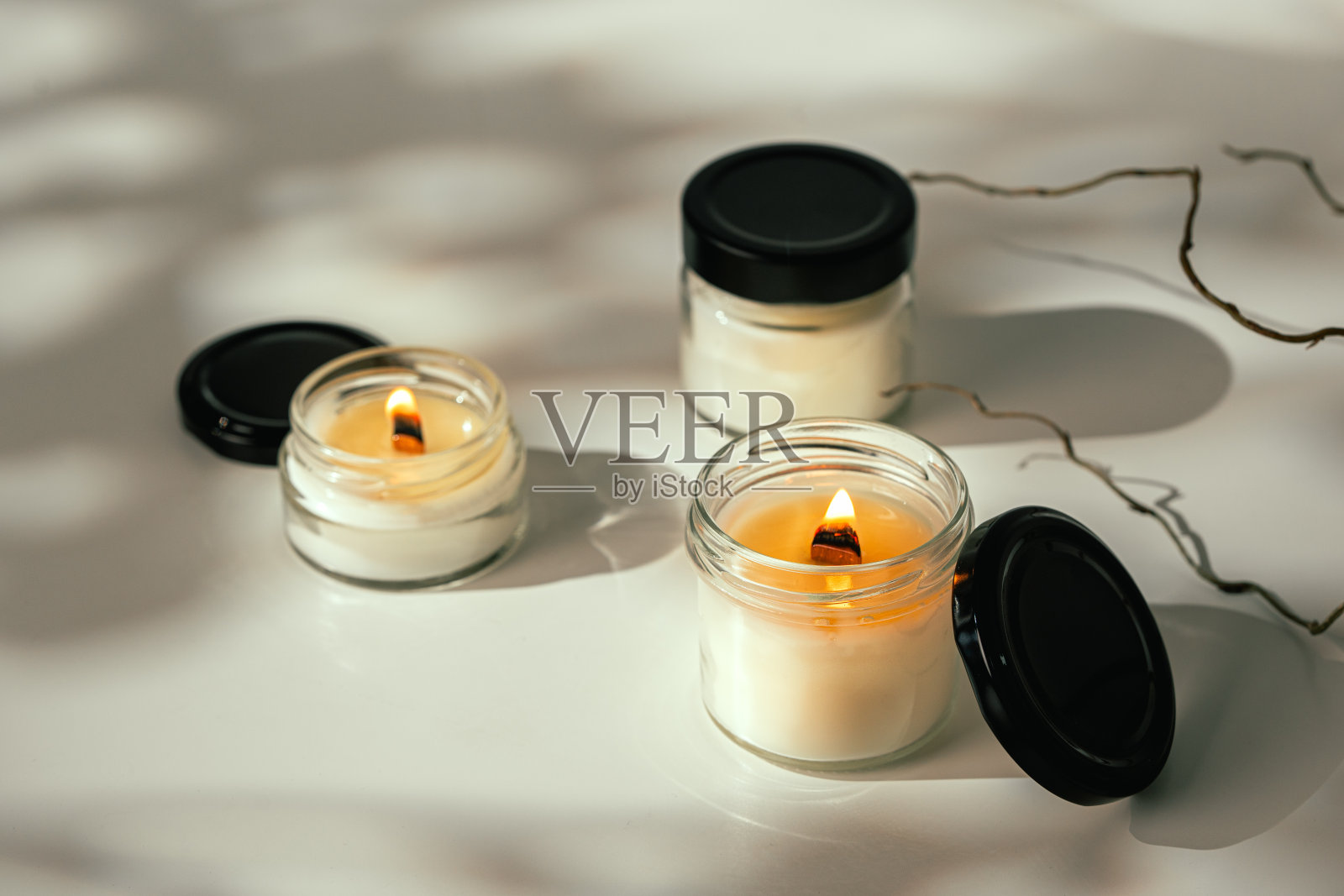 白色桌面上燃烧的玻璃罐蜡烛，树枝在阳光下照片摄影图片