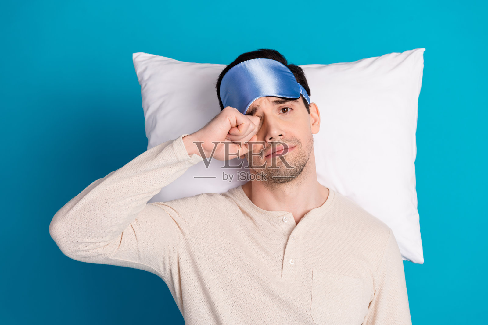 照片肖像英俊的年轻人躺着枕头累揉眼睛穿着睡衣过夜早上好孤立的蓝色背景照片摄影图片
