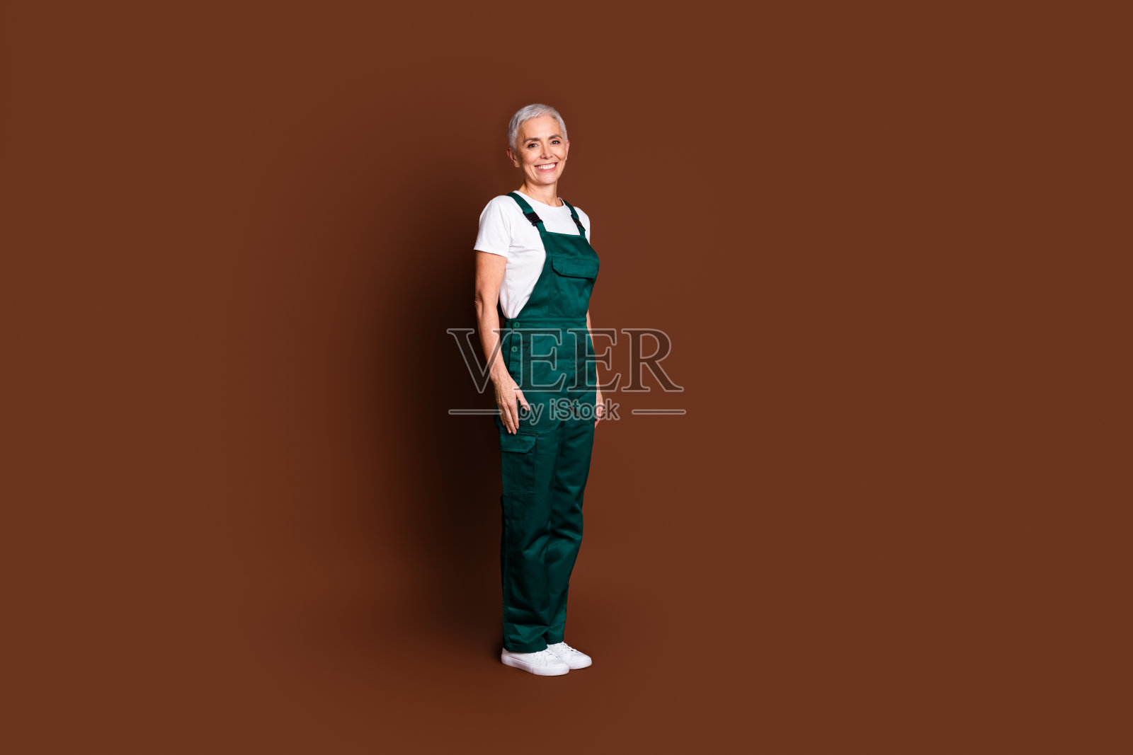 可爱的开朗的女人站在棕色背景的绿色整体孤立的全长照片照片摄影图片