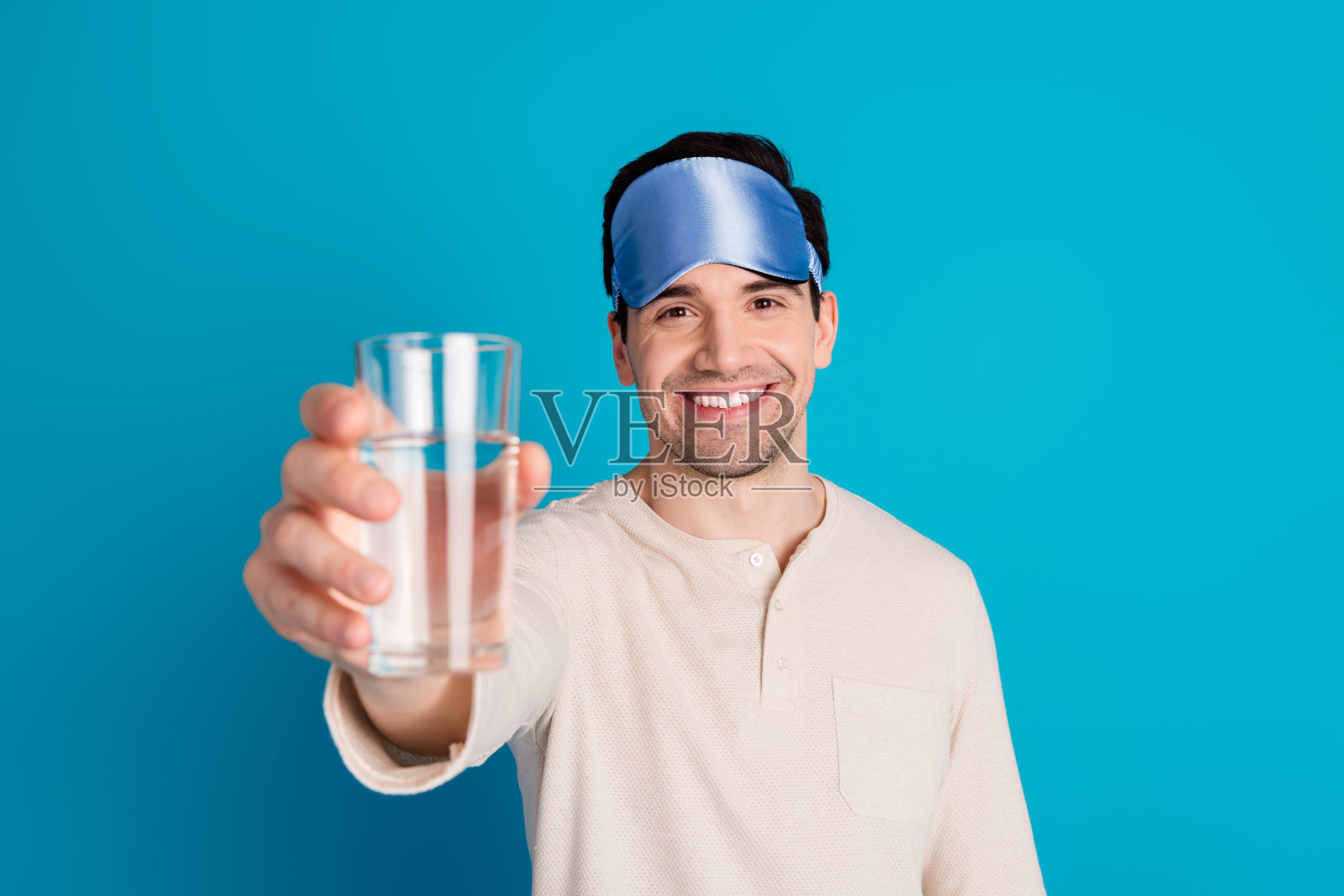 漂亮的年轻人的肖像拿着玻璃水穿着睡衣孤立的蓝色背景照片摄影图片