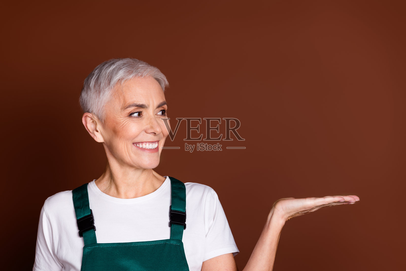 全身照片迷人的开朗的退休妇女穿着绿色工作服孤立的棕色背景照片摄影图片