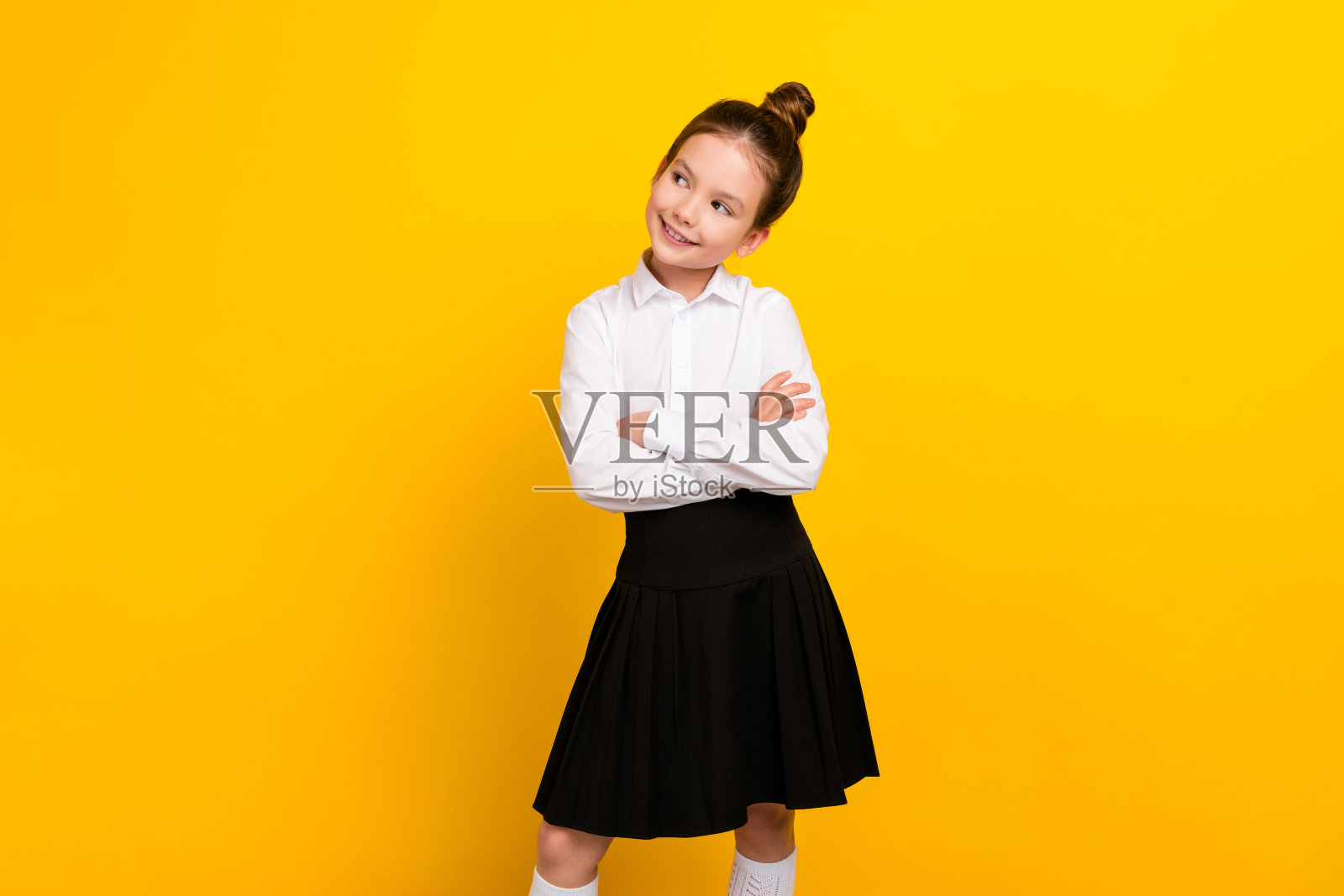 照片中可爱的女学生抱臂望空，穿着黄色背景上孤立的制服照片摄影图片