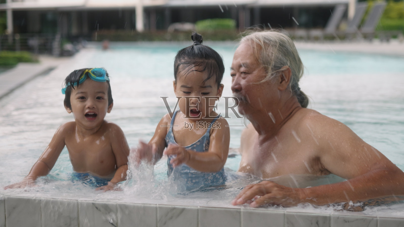 快乐的爷爷和他的孙子们坐在游泳池里玩耍。照片摄影图片