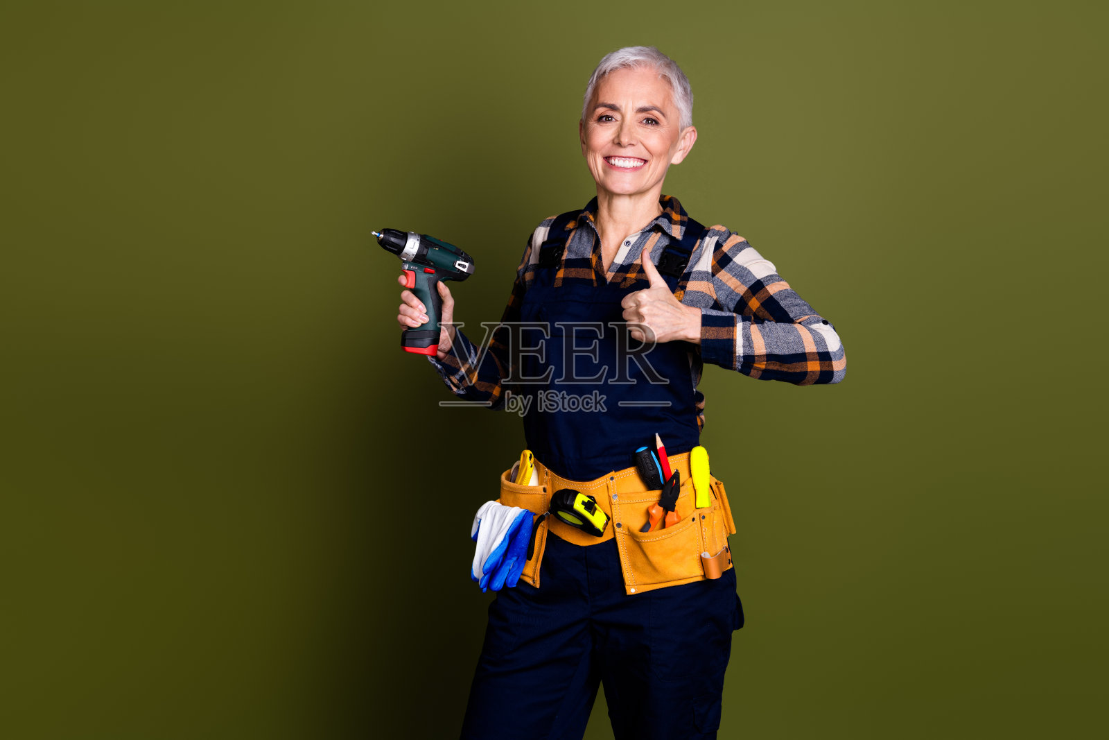 照片漂亮的资深女士专业专家杂工持有钻大拇指穿蓝色工作服整体孤立在卡其色背景照片摄影图片