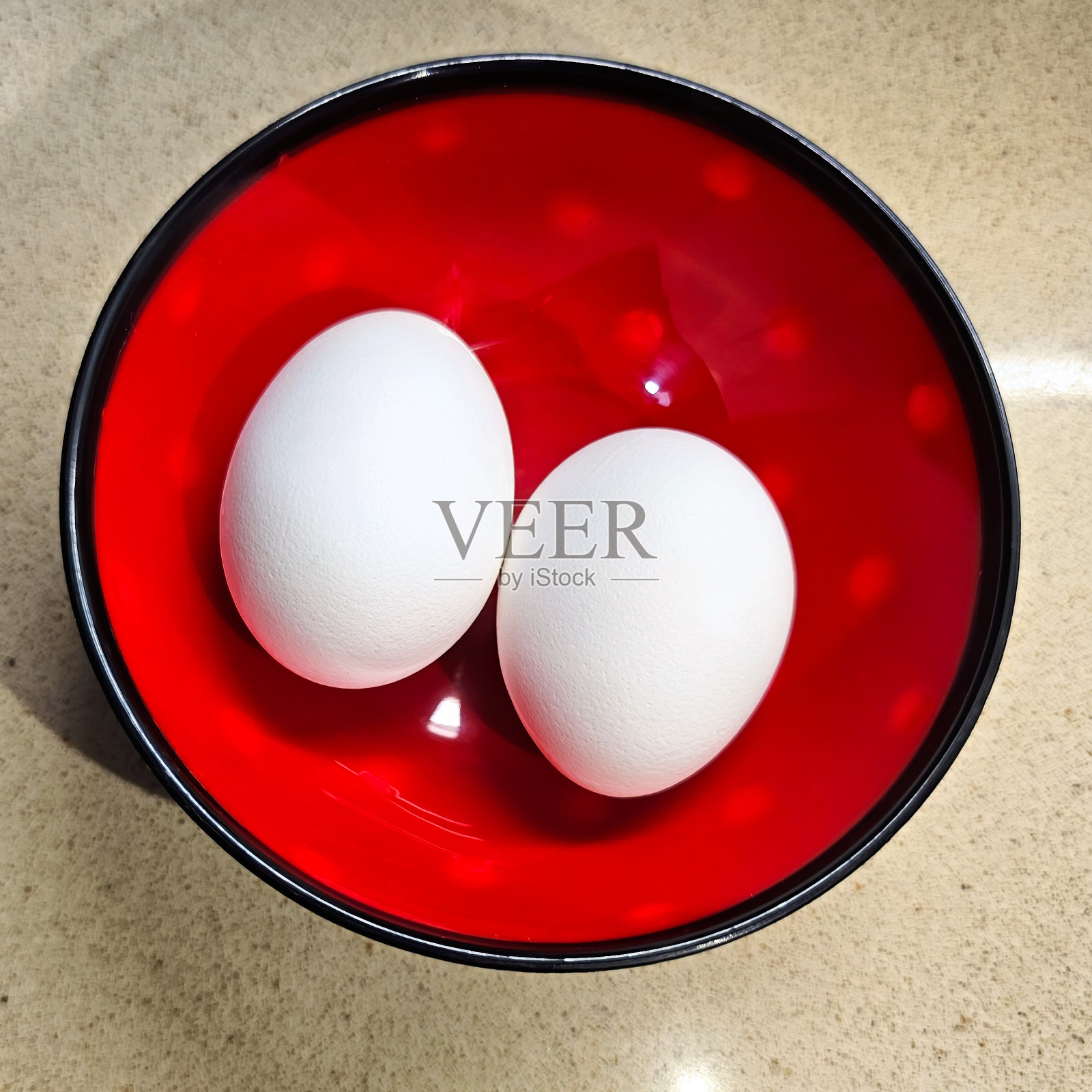 红色碗里放着两个未煮的白色鸡蛋，碗上有白色斑点照片摄影图片