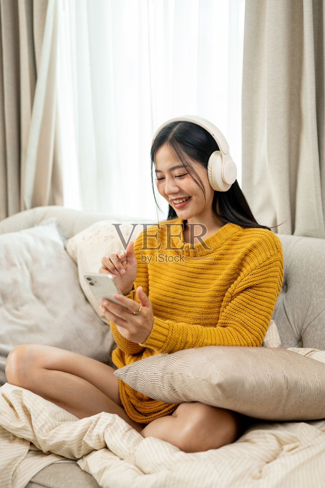 一位美丽、乐观的亚洲女性正坐在家里的沙发上享受着音乐。照片摄影图片