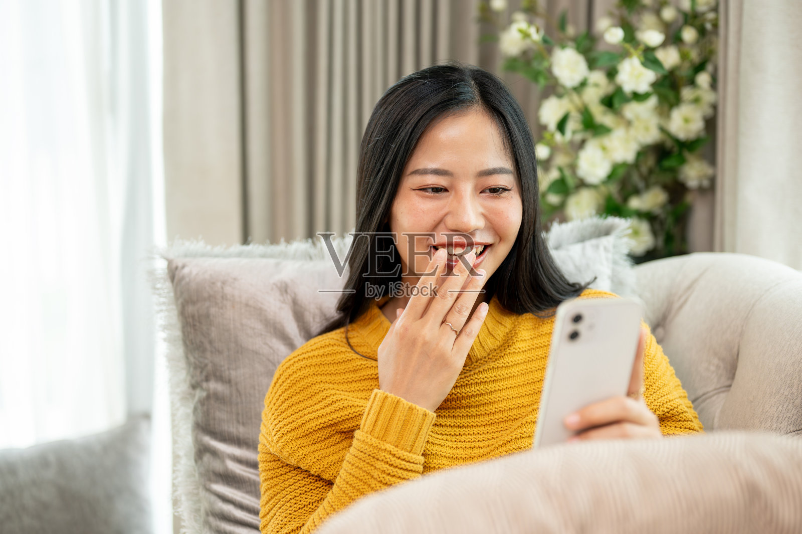 一位心情愉快的女士坐在家里的沙发上，用智能手机观看社交媒体(sns)上的视频。照片摄影图片