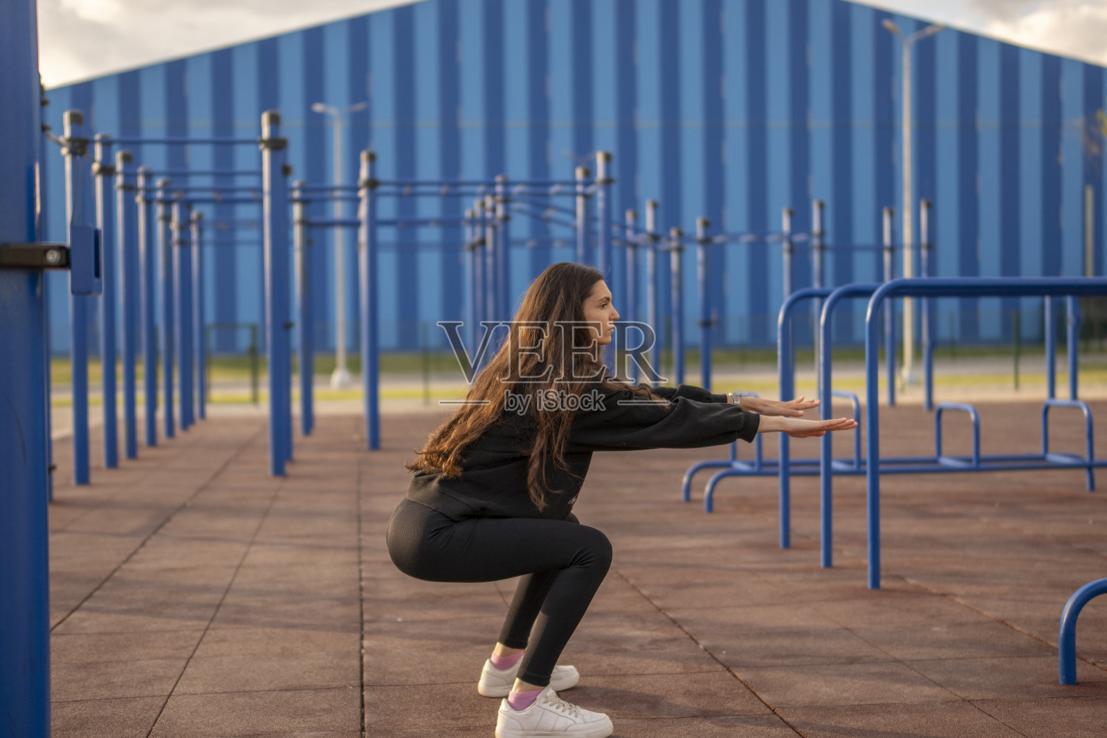 穿着运动服的女子在户外健身器材上做深蹲照片摄影图片