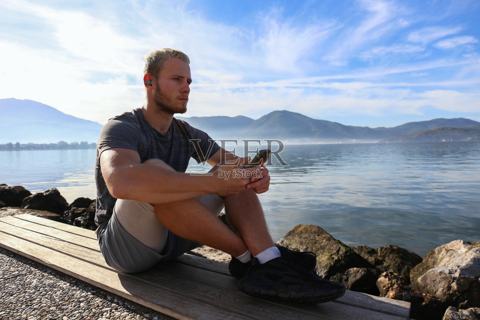 一个拿着电话的年轻人坐在人行道上。照片摄影图片