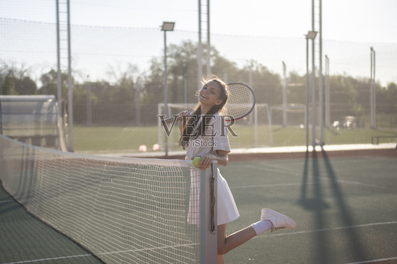 在一个阳光明媚的日子里，一名女子站在网球场附近，手里拿着网球拍照片摄影图片
