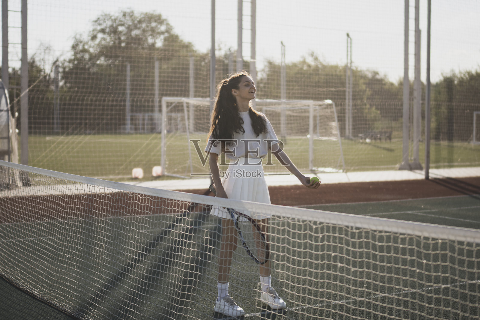 在红土球场上，一名身穿白色裙子和衬衫的女子拿着网球拍微笑着照片摄影图片