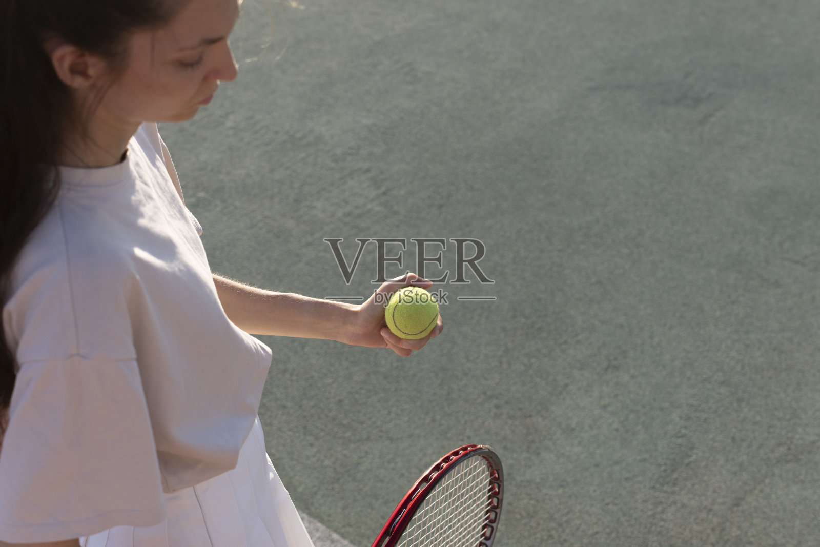 一名女子网球运动员站在网球场上，右手拿着一个网球。她穿着一条白色的裙子和一件浅灰色的t恤照片摄影图片