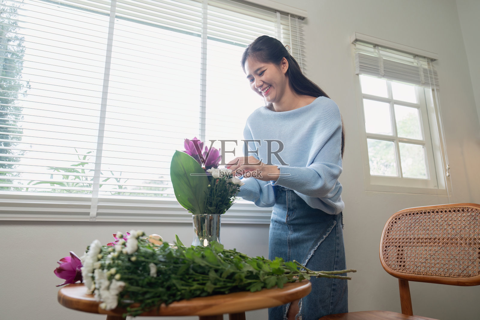 一名妇女在现代家庭的一扇阳光明媚的窗户前把鲜花插在花瓶里照片摄影图片