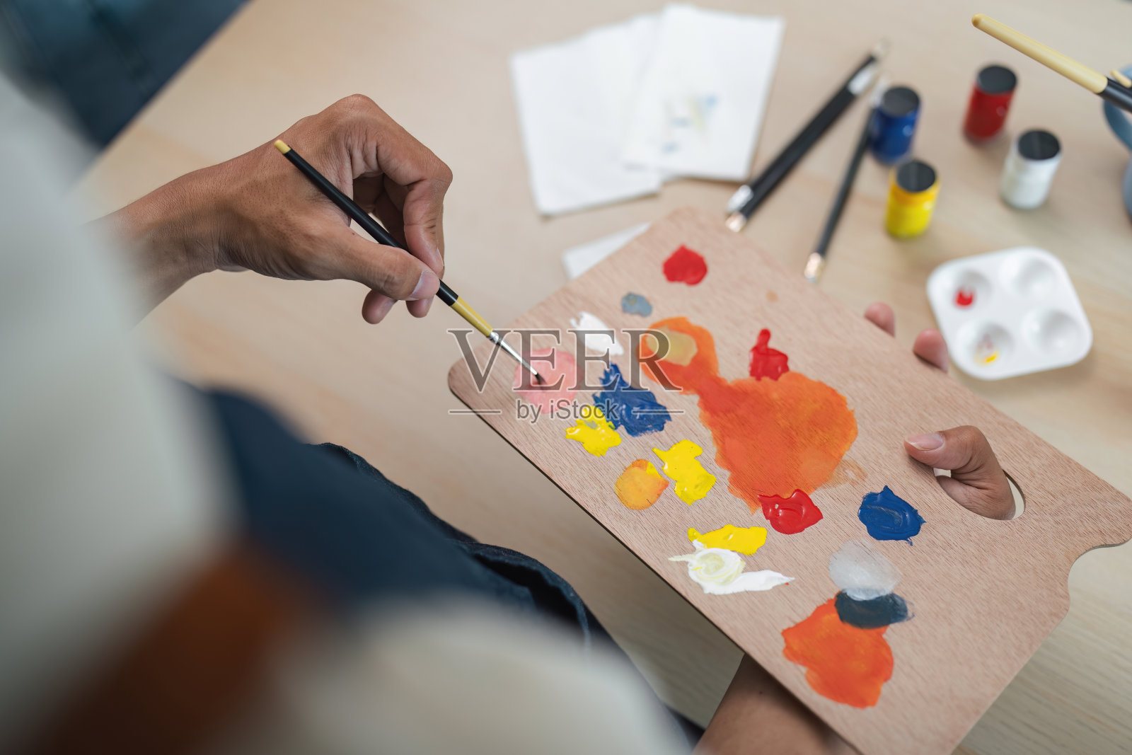 艺术家在调色板上与背景中的画笔和画布混合充满活力的油漆颜色照片摄影图片