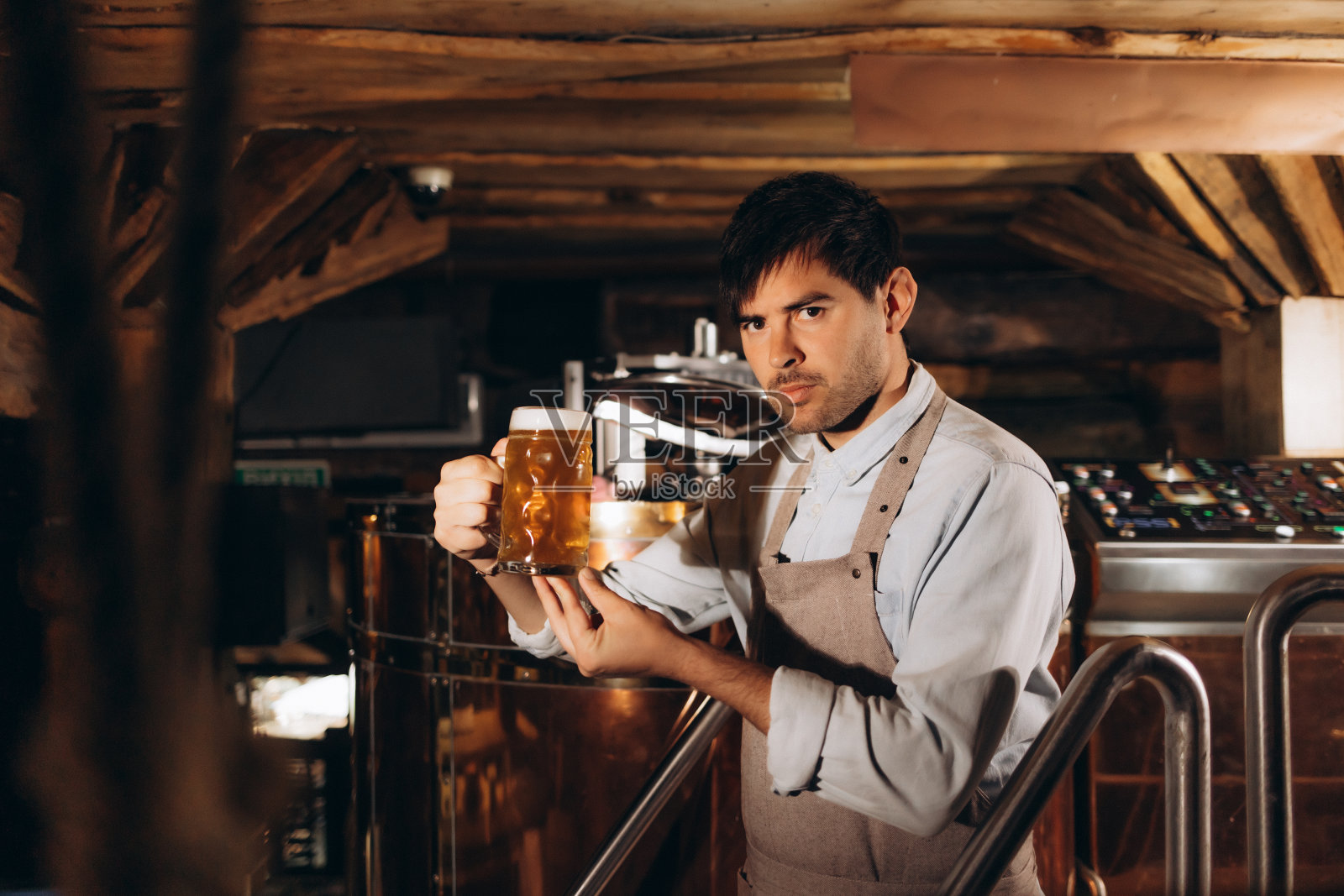 年轻人在啤酒厂检查精酿啤酒的质量。在酒精制造工厂检查啤酒的男检查员。照片摄影图片