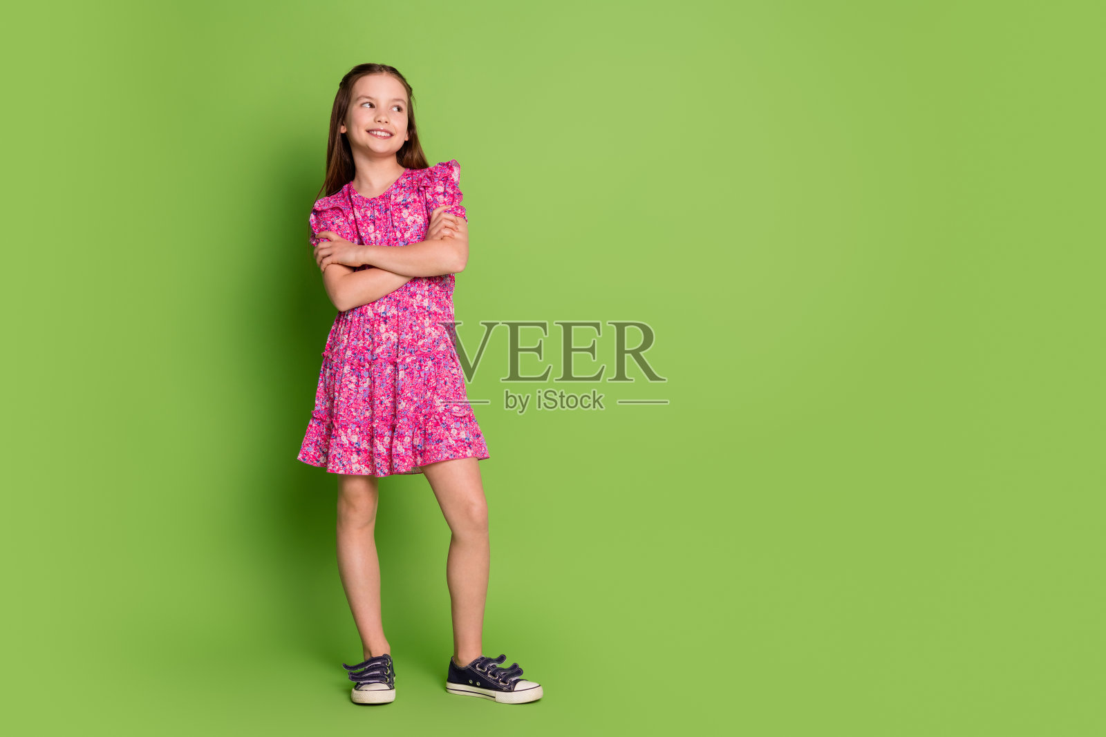 可爱的女学生的全尺寸照片，双臂交叉，看起来空无一物，穿着粉红色的裙子，孤立在绿色的背景上照片摄影图片